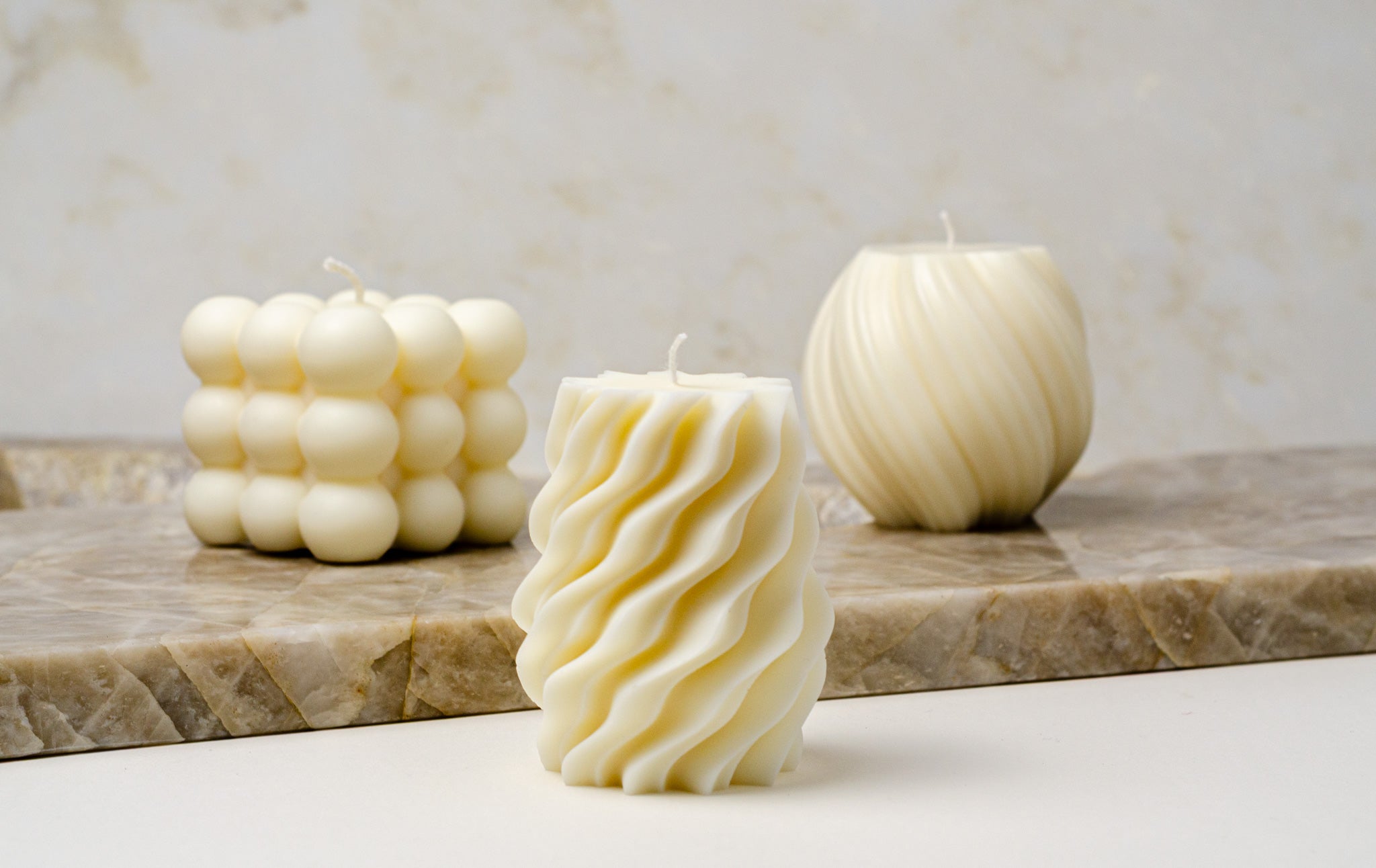 Trijų formų sojų vaško žvakės – Bubble, Helix ir Satori – ant natūralaus akmens paviršiaus